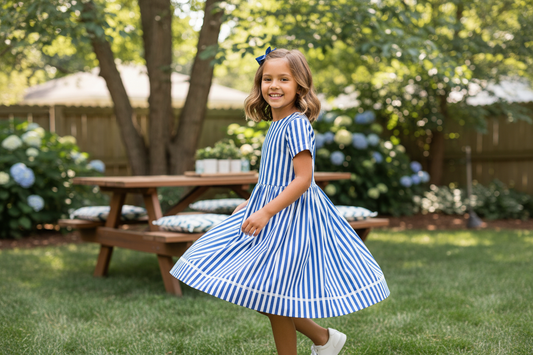 Smiling girl twirls in a blue and white striped dress, perfect for stylish girls’ summer outfits