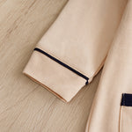 Beige cotton garment with dark blue piping and patch detail on wood.