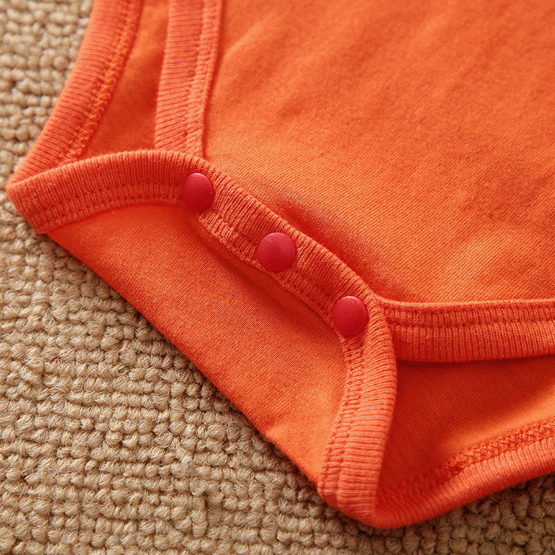 Close-up of an orange baby outfit with buttons on a beige carpet