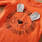 Orange shirt with a lion face design and gray mask attachments on a textured surface.