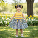 Happy young girl smiling in a butterfly dress for girls with a cheerful yellow top and striped floral skirt, set in a bright garden.