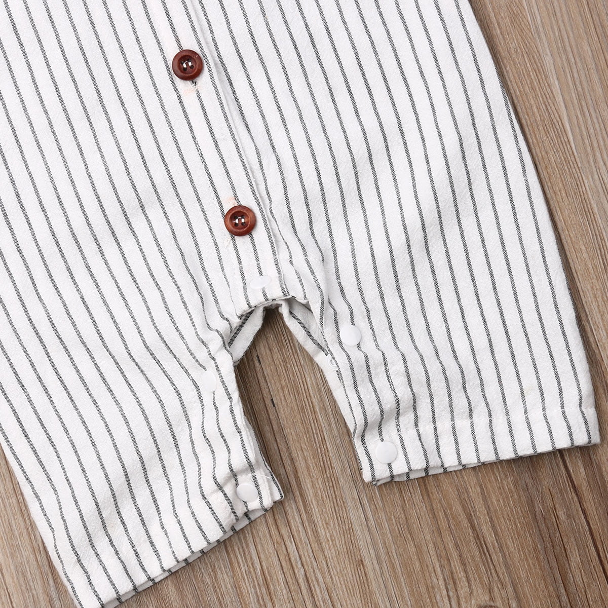 Close-up of a white and grey striped baby jumpsuit with brown and white buttons.