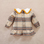 Back view of Plaid baby dress shirt with ruffled collar on a beige background