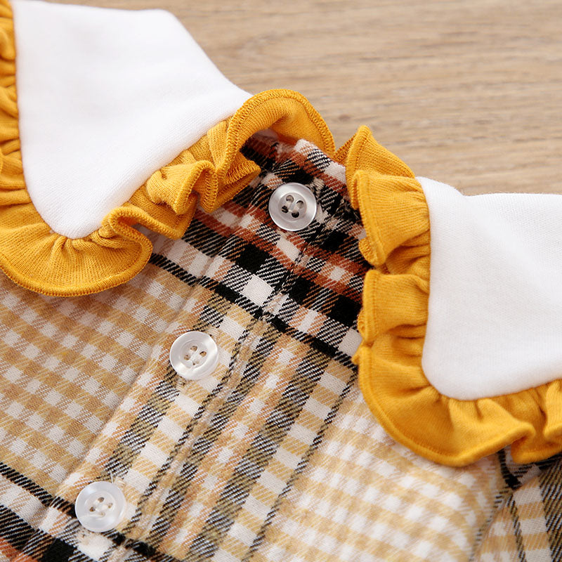 Close-up of a plaid garment with yellow ruffled trim and white buttons on a wooden surface.
