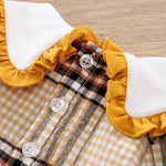 Close-up of a plaid garment with yellow ruffled trim and white buttons on a wooden surface.