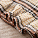 Close-up of plaid fabric with brown, black, and beige colors on a textured surface.