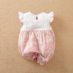 Baby romper with white top and pink floral bloomers on the bottom half on a beige background