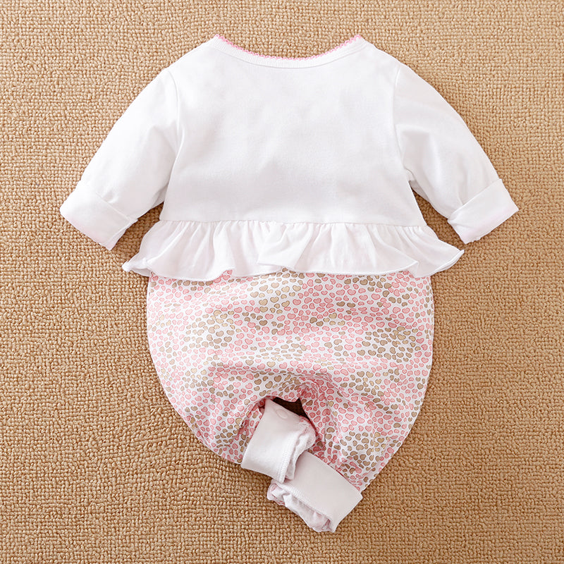 White and pink heart-patterned baby long-sleeve jumpsuit on a brown surface.