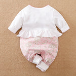 White and pink heart-patterned baby long-sleeve jumpsuit on a brown surface.
