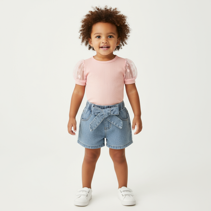 A happy child wearing cute kids clothing, showcasing a playful poke dot sleeve top paired with fashionable denim shorts, standing confidently in a bright white background.