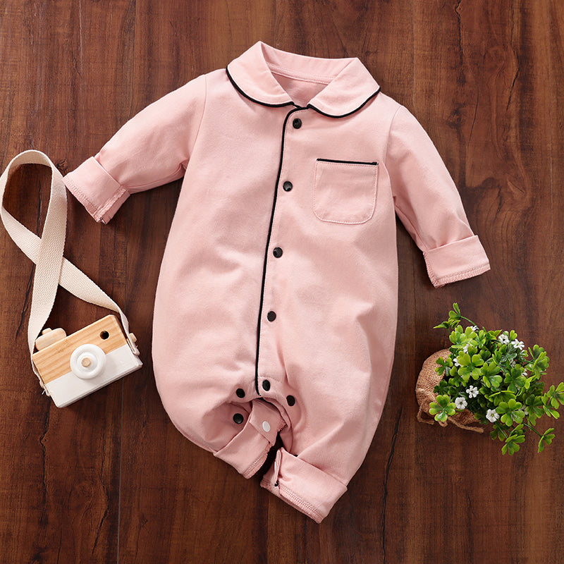 Pink baby cotton sleepwear with black snap buttons on a wooden surface, accompanied by a toy camera and small plant.