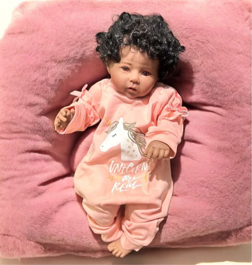 A delightful baby doll dressed in a unicorn shirt reclines on a plush pink pillow, capturing the essence of whimsical childhood joy.