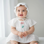 Baby Girl Cotton Romper Dress With Matching Hat featuring a happy baby sitting down, showcasing the soft, breathable fabric and floral design of the cotton romper dress.