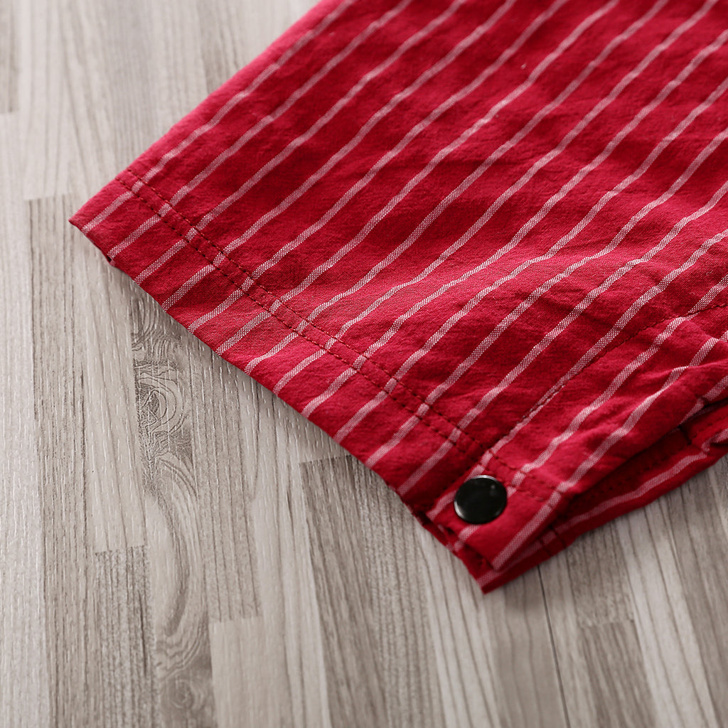A close-up of the hem of the Adorable 1-Piece Striped Infant Clothing Jumpsuit With Bow Tie & Button-Up Front, showing red fabric with thin white vertical stripes and a black button, lying on a light wood-grain floor.