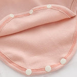Close-up of pink ribbed baby romper fabric with white snap buttons.