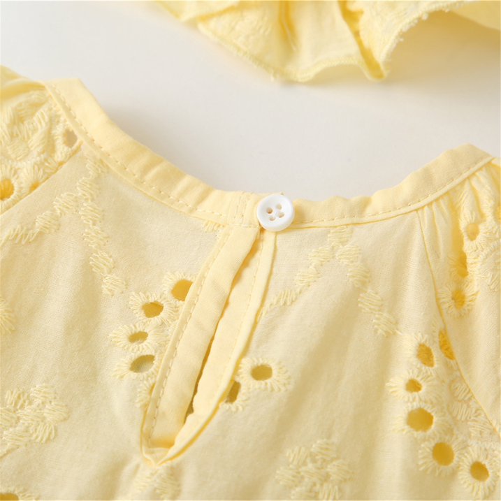 Close-up of a soft yellow cotton garment with eyelet embroidery and a white button.