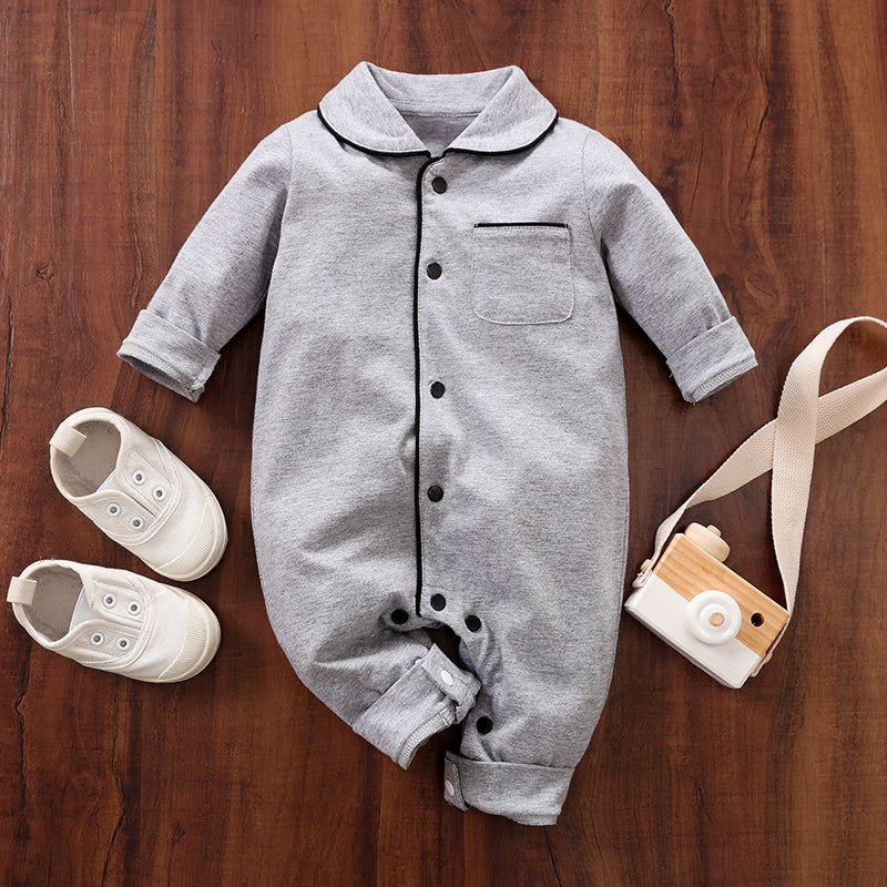 Gray baby pajamas with black snap buttons on a wooden surface, accompanied by white shoes and a small camera.