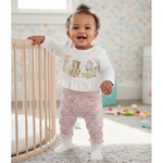 Happy baby girl wearing the Baby Girl Deer Heart Jumpsuit, Soft Cotton, Long Sleeve by Hushies, standing in a stylish nursery with a ruffled waist detail.