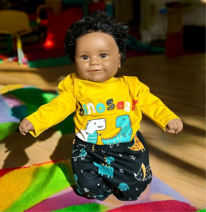 A cute doll dressed in a yellow shirt and black pants, showcasing a unisex dinosaur-themed baby outfit.  