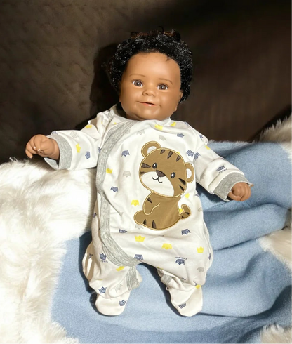 Adorable baby doll with a teddy bear on its chest, dressed in a king crown jumpsuit, radiating charm and warmth.