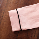 Folded pink fabric with a black edge on a wooden surface