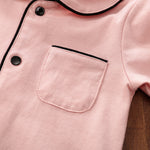 Close-up of a pink cotton sleepwear with black snap buttons and trim on a wooden surface