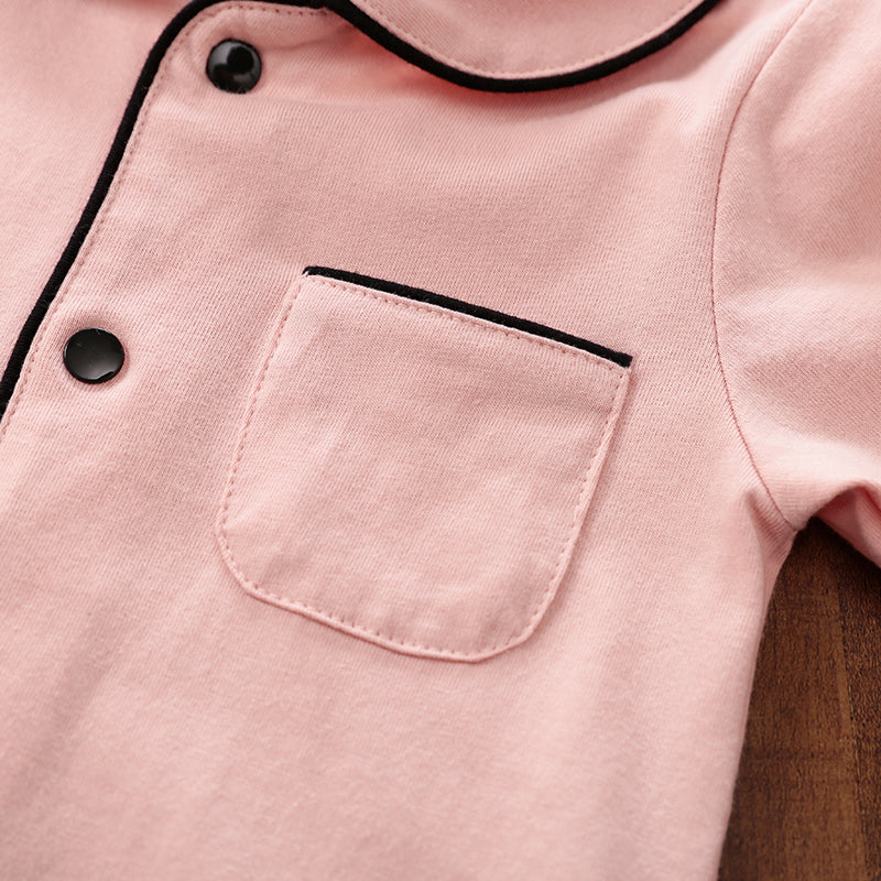 Close-up of a pink cotton sleepwear with black snap buttons and trim on a wooden surface