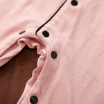 Close-up of a pink garment with black snap buttons on a wooden surface