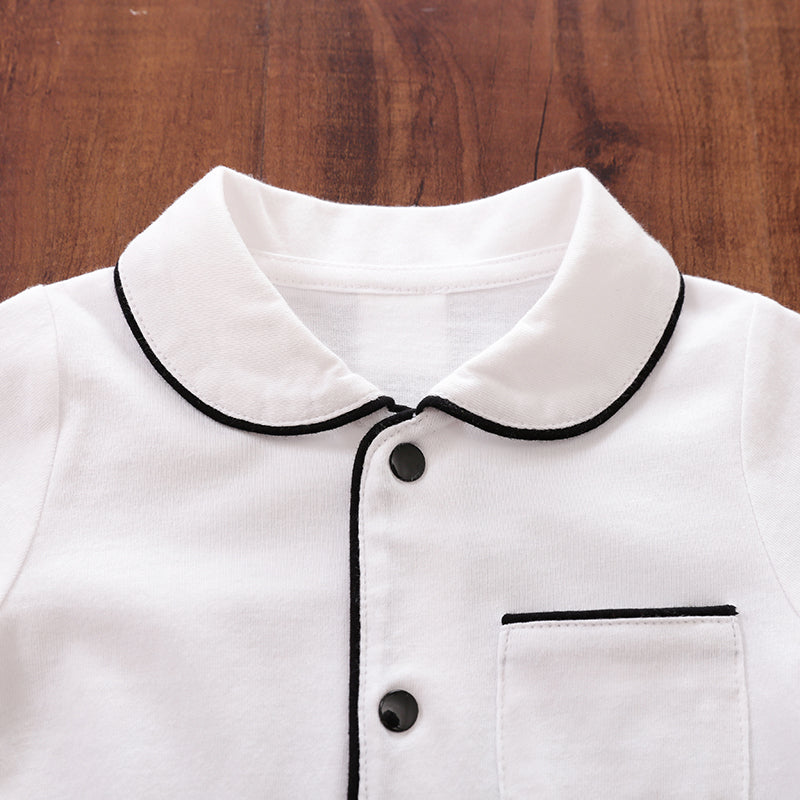 White baby sleepwear with black trim and snap buttons on a wooden surface