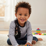 Smiling child sitting on a rug, dressed in Hushies Boys Lion Print Long Sleeve Shirt, perfect for playtime activities.